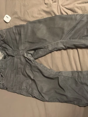 Grå jeans från G-Star RAW - Säljer ett par grå jeans från G-Star RAW med coola sömdetaljer och en avslappnad passform. Jeansen har fem fickor, bälteshällor och en snygg tvättad look. Perfekta för dig som gillar lite archive och vill ha något unikt i garderoben.