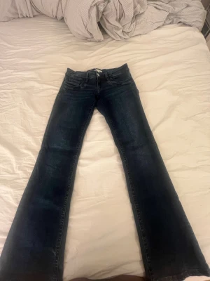 Mörkblå bootcut jeans - Säljer ett par mörkblå bootcut jeans med klassisk femficksdesign och snygga slitningar framtill. Jeansen har normal midja och är tillverkade i denim med lätt stretch. Perfekta för dig som gillar en avslappnad men ändå trendig look.