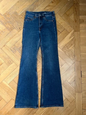Blå bootcut jeans med hög midja - Säljer ett par klassiska blå bootcut jeans i bra skick. Jeansen har en snygg utsvängd passform från knät och ner. 