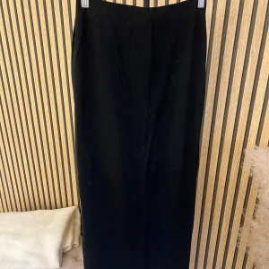 Svart långkjol med slits från H&M - Stilren svart långkjol med rak passform och diskret slits baktill. Kjolen har en minimalistisk design som gör den enkel att matcha med olika toppar och skor. Perfekt för dig som gillar en klassisk och tidlös look.