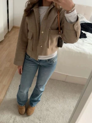 Beige jacka ifrån Zara - Snygg beige jacka i ull med stora fickor framtill och knappar. Kortare modell med krage och lång ärm, perfekt för lager på lager. Passar till både jeans och kjol för en trendig look.