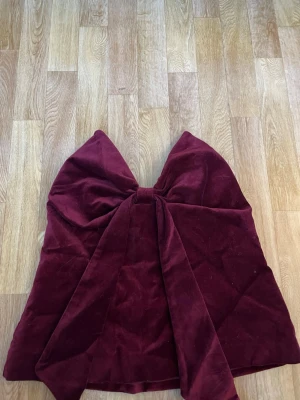 Vinröd sammets tubtopp med stor rosett - Supersnygg vinröd tubtopp i mjuk sammet med en stor rosett framtill. Toppen är axelbandslös och har en elegant, croppad passform som verkligen sticker ut. Perfekt för dig som vill ha något unikt och trendigt.