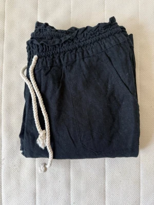 Roxy - Trousers, true black - Säljer ett par mörk blåa linnebyxor med bred resår i midjan och vit snörning. Byxorna har avslappnad passform och fickor framtill. Materialet känns mjukt och skönt, perfekt för våren och sommaren. Sälja då de är lite korta på mig - använt 2-3 gånger endast. Nypris: 500kr