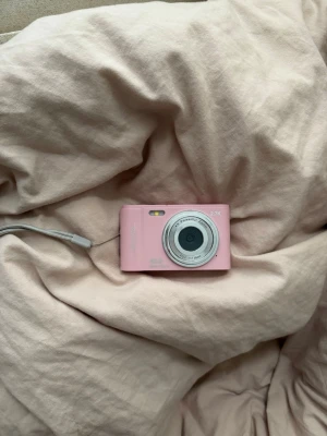 Rosa digitalkamera med handledsrem - Söt rosa digitalkamera med silverfärgat objektiv och tydlig display på baksidan. Kameran har en kompakt och smidig design, perfekt att ta med sig överallt. Utrustad med handledsrem för extra säkerhet. Passar dig som vill ha en enkel och snygg kamera.