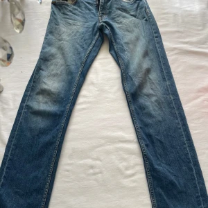 Blå jeansbyxor från Italien - Klassiska blå jeansbyxor med raka ben och normal passform. Byxorna har fem fickor, dragkedja och knapp framtill. Tillverkade i Italien och har en snygg tvättad look med lätt slitning på låren. 31/34