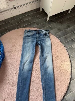 Ljusblå slim jeans från replay - Snygga ljusblå jeans från replay med slim fit och klassisk femficksdesign. Jeansen har slitningar och en tvättad look, samt replay ikoniska läderpatch bak i midjan. Perfekta för en avslappnad och trendig stil.