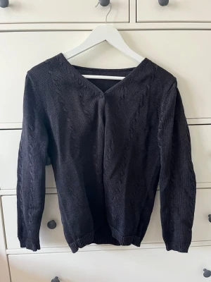 Mörkblå stickad kofta med knappar - Mörkblå stickad kofta med v-ringning och knappar. Koftan har diskreta mönsterstickningar och långa ärmar. Köpt secondhand i butik, ingen lapp men enligt mig storlek S/36. 