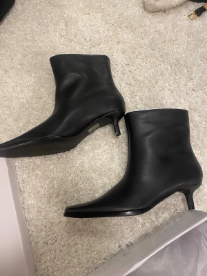 Svarta boots med låg klack - Stilrena svarta stövletter i slätt skinnimitation med spetsig tå och låg smal klack. Helt oanvända, köpta från Nelly.