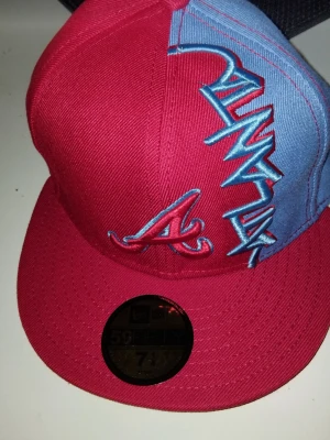 Atlanta Braves keps från New Era - Säljer en Atlanta Braves 59FIFTY keps från New Era. Kepsen är röd med ljusblå panel och har broderad Braves-logga samt texten 'Atlanta' i blått och vitt. Klassisk flat brim och sticker kvar på skärmen. Perfekt för dig som gillar sportig streetstyle.