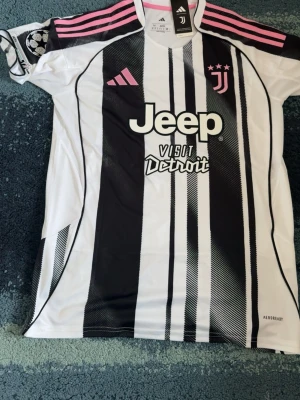 Juventus tröja kenan Yildiz - Juventus officiella matchtröja i svartvitt med rosa detaljer och Jeep-logga på bröstet. Tröjan har nummer 10 och namnet Yildiz på ryggen, samt Champions League-märke på ärmen. Tillverkad i lätt och ventilerande Aeroready-material.