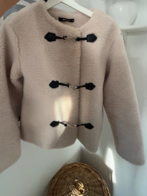 Beige teddyjacka med toggleknäppning - Supersnygg beige teddyjacka från Gina Tricot med tre svarta toggleknäppningar framtill. Jackan har en boxig passform, rundad krage och är gjord i mjukt, fluffigt teddy-material som håller dig varm under kalla dagar.