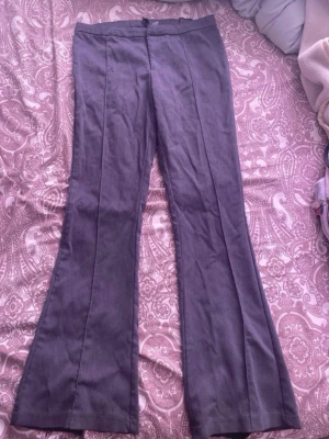 Grå kostymbyxor från H&M Divided - Snygga grå kostymbyxor från H&M Divided i storlek 40. Byxorna har utsvängda ben och pressveck framtill för en clean look. Tillverkade i ett mjukt tyg som känns bekvämt hela dagen. Perfekta för dig som gillar en stilren och trendig vibe.