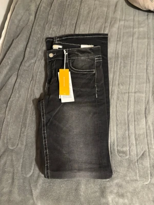 Svarta jeans med kontrastsömmar - Snygga svarta/gråa jeans med vita kontrastsömmar och klassisk femficksdesign. Jeansen är nya med prislapp och är ej använda. De är i storlek 170 men passar en som har 34. Perfekta för dig som vill ha en stilren men ändå cool look.