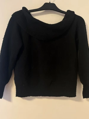 Svart stickad off shoulder tröja. - En svart stickad off shoulder tröja med långa ärmar. Tröjan har en avslappnad passform och är gjord i ett mjukt, fluffigt material som känns riktigt skönt. Perfekt för dig som gillar en enkel men snygg look.