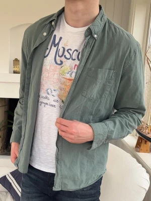 Acne studios skjorta - Stilren grön skjorta i bomull med klassisk knappkrage och bröstficka. Skjortan har långa ärmar och en relaxed passform som funkar till många olika looks. Perfekt att bära öppen över en t-shirt eller knäppt för en mer uppklädd stil.