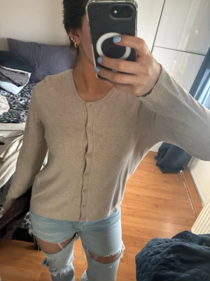 Beige kofta från KappAhl, storlek M - Snygg beige kofta från KappAhl i storlek M. Den har rund hals, långa ärmar och knappar framtill. Materialet känns mjukt och lätt, perfekt för lager-på-lager. Enkel och stilren design som funkar till många olika looks.