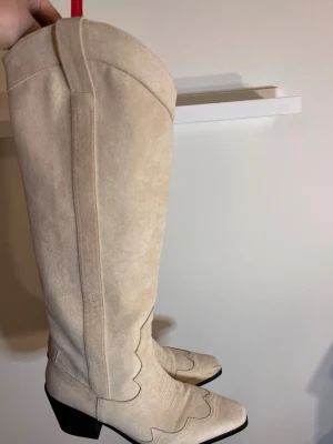  cowboy boots 40 - Säljer ett par snygga beige cowboy boots i mocka med spetsig tå och markerad klack. Använda en gång