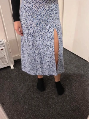 Långkjol - Säljer en blå långkjol med vitt blommönster och en snygg slits framtill. Kjolen har en rak passform.