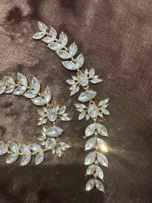 Glittrig kristallväst i guldton armband med hårsmycken💛 - Unikt hårjuveler ger en gnistrande och lyxig känsla som är perfekt för festival, bröllop, nyårsfester eller alla tillfällen där du vill vara kvällens stjärna.Säljer  glittriga, bladformade kristaller i silverfärg på guldfärgad metall. 