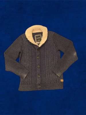 Mörkgrå kofta med fuskpäls från Raphael - Säljer en mörkgrå kofta från Raphael med grovstickat mönster och stora knappar framtill. Kragen är fodrad med mjuk beige fuskpäls som ger extra mysfaktor. Perfekt för kyliga dagar och har långärmad passform.