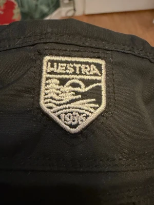 Hestra vantar - Säljer ett par svarta Hestra tumvantar med broderad logga och elastisk mudd. Utsidan är i slitstark syntet och handflatan i mjukt skinn. Insidan är fodrad för extra värme och komfort. Perfekta för kalla vinterdagar och outdoor-äventyr.
