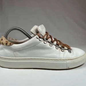 Vita diemme skor med leoparddetalj - Unika vita sneakers i skinn med bruna snören och metallhål för snörning. Skorna har en cool leopardmönstrad detalj vid hälen och platt sula. Insidan verkar vara fodrad med päls för extra komfort och stil.