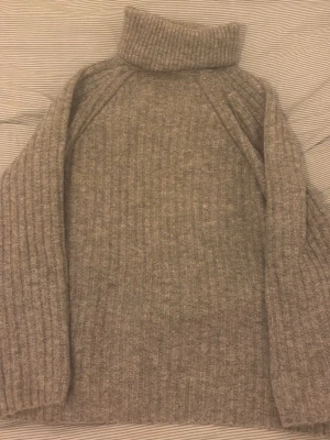 Grå stickad polotröja  - Mysig grå polotröja med ribbad struktur och lång ärm. Tröjan är stickad och har en hög polokrage som håller dig varm under kyliga dagar. Perfekt för lager på lager och enkel att styla till jeans eller kjol. 