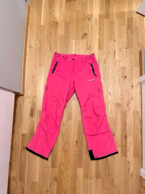 Rosa täckbyxor från 8848 Altitude - Snygga rosa täckbyxor från 8848 Altitude med svarta dragkedjor och förstärkta benslut. Byxorna har flera fickor med dragkedja och justerbar midja. Perfekta för vinterns alla äventyr i backen eller snön. Liten fläck på ena benet, inte försökt ta bort! Bild 1+2 visar färgen bäst 😍🩷