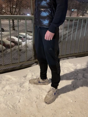 Svart dunväst från Moncler med huva - Säljer en svart glansig dunväst från Moncler med avtagbar huva och dragkedja framtill. Västen har två fickor med dragkedja och klassisk Moncler-logga på bröstet. Perfekt för lager-på-lager och riktigt snygg till streetwear.