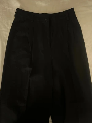 Svarta kostymbyxor från BikBok - Klassiska svarta kostymbyxor från BikBok i rak modell. Byxorna har hög midja. Tillverkade i ett mjukt och följsamt material som ger en clean och stilren look. Har kommit till användning 1 gång. 