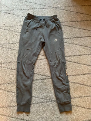 Grå mjukisbyxor från Nike - Säljer ett par grå mjukisbyxor från Nike med dragsko i midjan och ribbade muddar vid bensluten. Byxorna har två fickor framtill och en liten Nike-logga på låret. Perfekta för chill eller träning. Skrynkliga då dom legat i garderoben men är som nyskick 