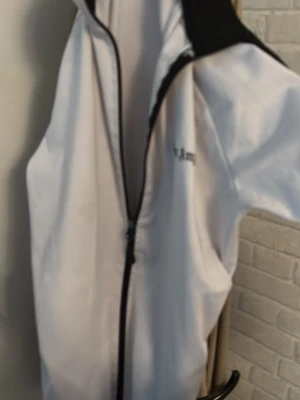 Vit  Palm Angels XL - Säljer en clean vit  från Palm Angels i storlek XL. Jackan har svarta detaljer längs dragkedjan och axlarna, samt Palm Angels-logga på bröstet. Hög krage och två sidofickor. Perfekt för dig som gillar streetwear och sportig stil.