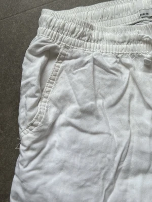 Vita linnebyxor från 157 - Säljer ett par vita linnebyxor från 157 med resår i midjan och dragsko. Byxorna har raka ben, sidfickor och är tillverkade i ett lätt och luftigt linnematerial. Perfekta för varma dagar och chill stil.