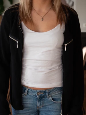 Svart stickad kofta med dragkedjor - Svart stickad kofta med hel dragkedja framtill och två coola bröstfickor med dragkedjor. Långärmad och i mjukt material som passar perfekt till jeans. Enkel och stilren design som funkar året runt.