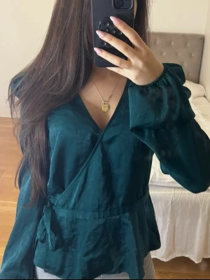 Blus från BIKBOK - Vacker mörkgrön blus som man knyter runt midjan. Har ett skönt satinmaterial. Kommer i storlek S men passar även XS.