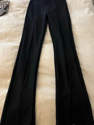 Svarta kostymbyxor med sömm och slits  - Säljer ett par svarta kostymbyxor i thights modell byxor från Gina Tricot i storlek XS. Byxorna har hög midja, slits framtill vid bensluten, och sömm längst benen. 