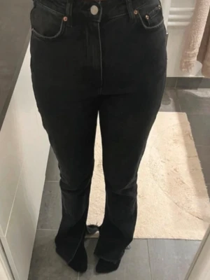 Svarta högmidjade jeans med slits  - Säljer ett par svarta högmidjade jeans med slits nertill. Jeansen har en rak modell, med avklippta ben nertill. Materialet är jeans och färgen är en snygg mörk svart. 