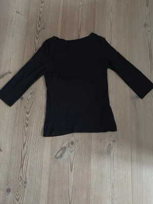 Svart topp med trekvartsärm Vero Moda - En stilren svart topp från Vero Moda med trekvartsärm och rund halsringning. Enkel och klassisk design som passar till många olika outfits. Tillverkad i ett mjukt och stretchigt material för en bekväm passform. 