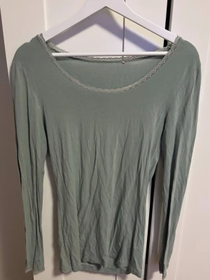 Ljusgrön/turkos långärmad topp med spetskant - Säljer en ljusgrön/turkos långärmad topp med rund halsringning och fin spetskant runt halsen. Storlek står inte men skulle säga S/M