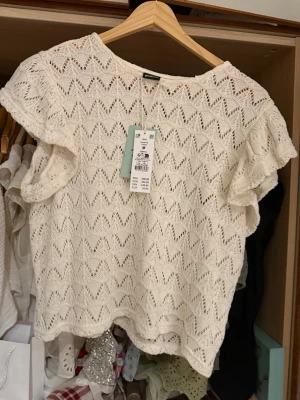 Vit virkad topp från Gina Tricot - Säljer en superfin vit virkad topp från Gina Tricot i storlek M. Toppen har korta ärmar med volangkant och ett snyggt hålmönster i zickzack. Perfekt till sommaren och lätt att styla med jeans eller kjol.