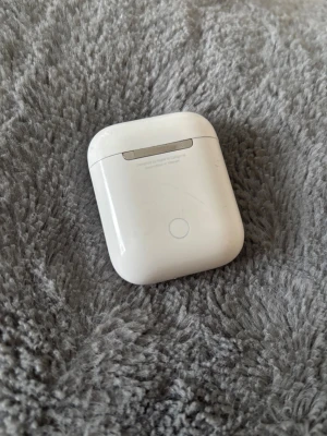 Apple AirPods (2nd generation) - Apple AirPods (2nd gen) med laddningsetui. Trådlösa hörlurar med smidig anslutning till iPhone och andra Apple-enheter. Viss yttre slitage och repor syns på både etui och hörlurar, men fungerar som de ska.