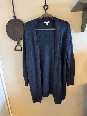 Mörkblå kofta i mjuk mix, stl S - Mysig mörkblå kofta med öppen front och lång ärm. Tillverkad i en mjuk blandning av akryl, polyamid, polyester, elastan och lite ull. Perfekt att slänga på sig när det är kyligt ute. Enkel och stilren design som funkar till det mesta.