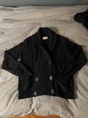 Svart kofta från Ralph Lauren M - Svart kofta från Denim & Supply Ralph Lauren i storlek M. Dubbelknäppt med sex knappar framtill och bred ribbad krage. Tillverkad i 100% bomull, med långa ärmar och ribbade muddar. Perfekt för lager-på-lager och chill stil.