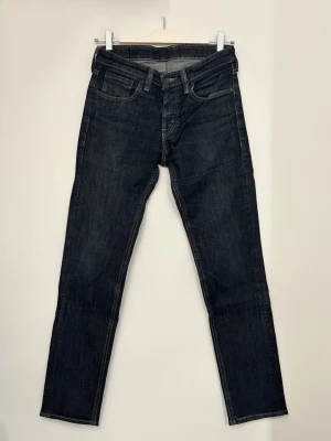 Levi's 511 mörkblå jeans W30 L32 - Snygga Levi's 511 jeans i mörkblå tvätt med klassiska fem fickor och gul kontrastsöm. Modellen är slim och har en rak passform med normal midja. Tillverkade i slitstarkt denimtyg som ger en tidlös look. Perfekta för dig som gillar stilrena och bekväma jeans.