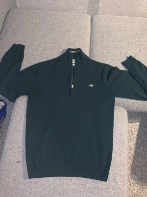 Mörkgrön half zip tröja från Gant - Säljer en mörkgrön långärmad tröja från Gant i superfin lammull. Tröjan har half zip-dragkedja, liten broderad logga på bröstet och ribbade muddar. Perfekt till höst och vinter för en clean och stilren look.