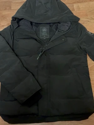 Svart Canada goose jacka - Stilren och diskret Canada Goose-jacka med helsvart label för en clean och exklusiv look. Jackan är varm, bekväm och gjord för kallt väder. En tidlös modell som passar perfekt till både vardag och mer uppklädda outfits.