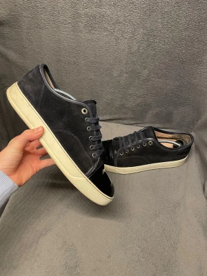 Marinblå Lanvin - Säljer ett par svarta sneakers från Lanvin med ovandel i marinblå mocka och svart lackad tå. Skorna har små defekter som knappt märks men dom har andvänds ett fåtal gånger. Skorna har storlek 42 men passar också 43. Nypris ligger runt 6000. Köpta på NK och kvitto, dustbag och box finns kvar.                                                        Skriv vid frågor, priset är inte hugget i sten🤝