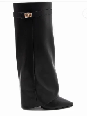 Svarta stövlar med spetsig tå - Säljer ett par svarta stövlar med spetsig tå och hög skaft. Skorna har en elegant guldfärgad detalj vid kanten och är tillverkade i skinn. Stövlarna har en cirka 10 cm klack och en stilren design som sticker ut.