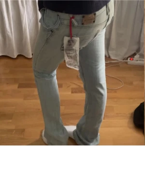  ljusblå bootcut jeans - Snygga ljusblå jeans med klassisk bootcut passform. Jeansen har fem fickor, dragkedja och knapp framtill samt detaljerade bakfickor. Materialet är jeans med en mjuk känsla och de har en lågmidjad design. Perfekt för dig som gillar en avslappnad stil.
