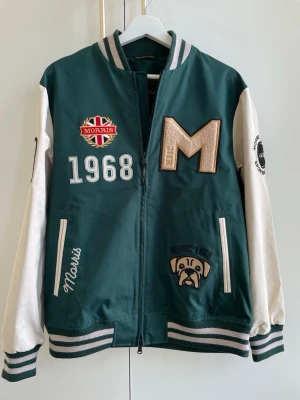 Morris bomberjacka - Ramsey jacket - Helt ny, lappen hänger kvar! Snygg bomberjacka från Morris i grönt och vitt med broderade patches. Jackan har randiga muddar, dragkedja och coola detaljer på ärmarna. Perfekt för dig som vill sticka ut med sportig stil. Passar dig som är ca 175 cm lång. 
